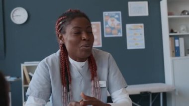 Afro-Amerikan kadın doktor, çocuk kliniğinde kızının tıbbi muayenesinden sonra tanınmayan bir babayla konuşuyor.