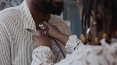 Doktor muayenehanesinde steteskopla oynarken babasının ciğerlerini dinleyen küçük kızın yakın plan fotoğrafını çek.