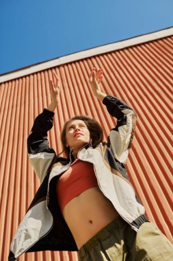 Kırmızı bir duvara karşı el kaldıran, spor giysileri giyen ve canlı bir arka plana karşı duran, muhtemelen egzersiz yapan ya da esneme hareketleri yapan insanlar.