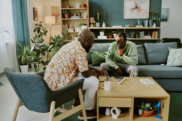 stock image Two modern African American male millennials spending spare time playing chess at coffee table in living room