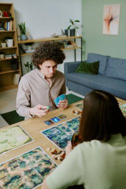 Masada oturan ve kız arkadaşıyla masa başında zar atan melez bir gencin dik açılı görüntüsü.
