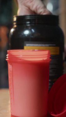 Vücut çalışmasından önce sütüne bir kaşık protein tozu ekleyen tanınmayan bir kadının dikey yakın çekimi.