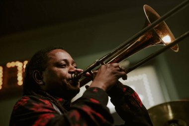 Barda canlı performans sırasında Afrikalı Amerikalı erkek müzisyenin trombon çalarkenki düşük açılı görüntüsü.
