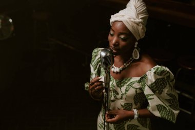 Sahnede mikrofonla şarkı söyleyen, şık giyinmiş, Afro-Amerikan bir kadının yüksek açılı görüntüsü.