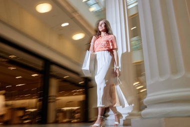 Pamuk bluz ve ipek etek giymiş alışveriş merkezinde alışveriş yapan genç bir kadının düşük açılı görüntüsü.