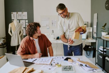 Tasarımcısı bakarken elinde bej kumaş parçası tutan olgun bir terzi.