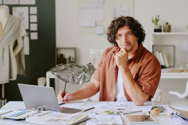 Yetenekli tasarımcı masada oturuyor ve atölyede çalışırken resim için poz veriyor.