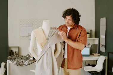 Kıvırcık saçlı terzi kendi atölyesinde yepyeni bir elbise üzerinde çalışıyor.