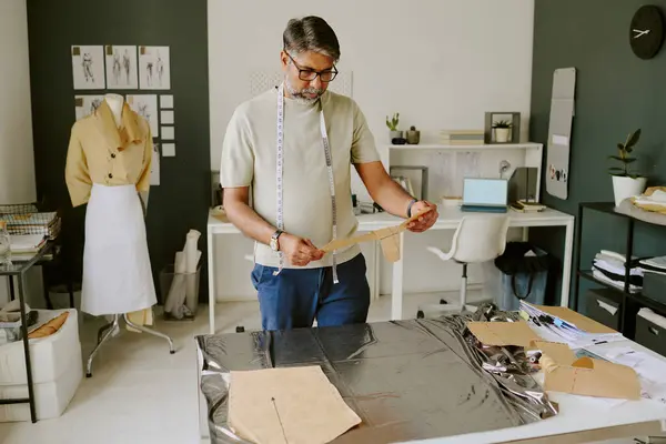 stock image Mature Indian tailor holding cotton stencil in hands and looking at it while creating metallic dress