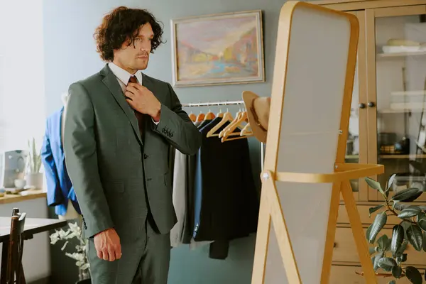 stock image Brutal man adjusting wine colored tie in front of mirror white in atelier fitting suit