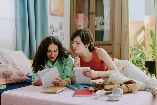 stock image Two friends sitting on a comfortable bed, engaged in studying with notebooks, pens, and other study materials spread around them