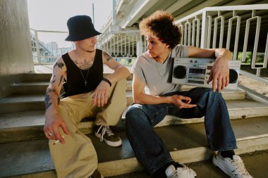Çift ırklı kardeşler merdivenlerde oturup sigara içiyor ve müzik dinliyor.