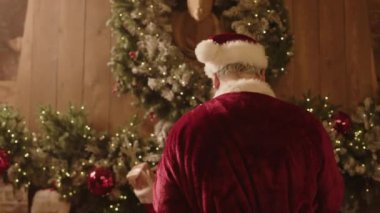 Noel Baba rolündeki yaşlı, beyaz bir adam Noel arifesinden önce çocuklar tarafından asılmış çorapları küçük hediyelerle ve hediyelerle taşıyor.