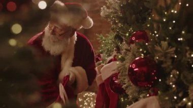 Noel Baba kostümü giyen orta yaşlı beyaz bir adam geleneksel olarak çocukların Noel çoraplarına küçük hediyeler ve hediyeler koyarken.