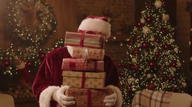 Noel Baba kılığına girmiş, elinde hediye kutuları olan, sihirli Noel atmosferinde kameraya poz veren ve gülümseyen neşeli beyaz adamın portresi.