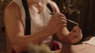 Kutlamaya hazırlanan fırçayla ahşap Noel süslerini boyayan neşeli, yaşlı, beyaz bir adamın orta boy yakın çekimi.