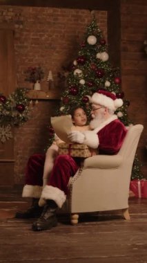 Dikey olarak Noel Baba 'nın kucağına oturmuş gelecek yıl için dilek ve umutlardan bahseden küçük bir kız resmi. Arka planda Noel ağacı ve şenlik süslemeleri.