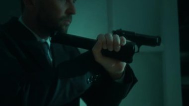 Resmi giyinmiş bir polis memuru dikkatle suç mahalline giriyor. Elinde tabanca ve el feneri var.