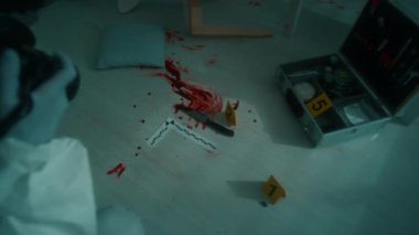 Olay yerindeki kan lekelerini ve bıçakları fotoğraflarken profesyonel kamerayla parlayan koruyucu tulumlar ve tek kullanımlık eldivenler giyen adli tıp müfettişinin omzunun üstünden.