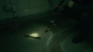 Dedektifin bıçak, kan lekeleri ve tebeşirle kurbanların cesedini karanlık odada fenerle incelerken meslektaşı da olay yeri incelemesi sırasında notlar alıyor.