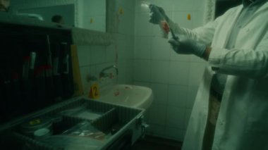 Beyaz önlüklü ve eldivenli suç mahalli teknisyeninin, plastik poşetteki kanıtları incelerken ve loş ışıklı tuvalette kan lekeli duvarlarla çalışırken görüntüsünü kaydederken.