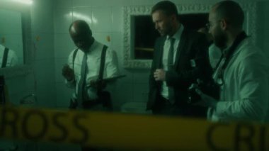 Kıdemli Afro-Amerikan dedektifi CSI ekibiyle kanıt tartışıyor ve bantlanmış loş bantları inceliyor.