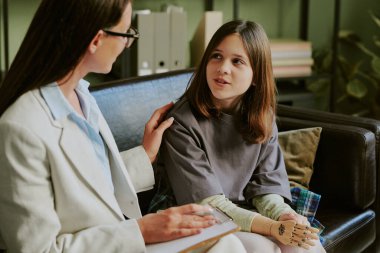 Protez bacaklı genç bir kız kanepesinde terapistle takılıyor iyileşme ve gelecek adımlara odaklanıyor dostane bir ortamda kişisel ilerlemeyi tartışıyorlar.