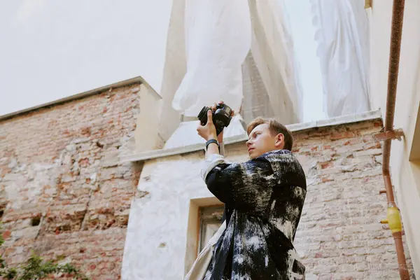 stock image Man operating a handheld gadget while capturing images of tall buildings. Puffy white clouds in the background with rustic brick buildings surrounding him