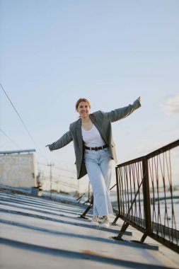 Kadın çatıda yürümekten zevk alıyor. Gün ışığında kollarını açmış, gülümsüyor. Rahatlamış ve mutlu bir ruh hali içinde.
