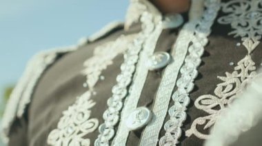 Güneşli bir günde açık havada duran, gümüş işlemeli ve düğmelerle süslenmiş siyah üniformalı bir adamın, eğik pozunu çek.