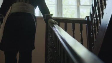 Periyot üniformalı, beyaz eldivenli, parmaklıklarda el ele tutuşan ve aşağı kata kameraya doğru yürüyen tanınmayan memurun yakın görüntüsü.