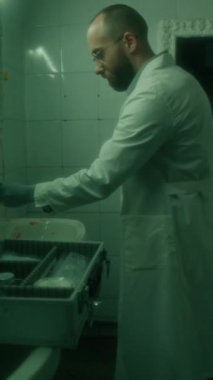 Olay yerindeki loş banyoda parmak izlerini incelerken beyaz önlüklü ve eldivenli adli tıp uzmanının dikey görüntüsü.