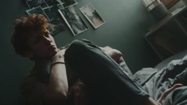 Stresli genç adam koyu gri duvarın yanında, üzerinde resimler ve yastıkla oturuyordu.