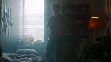 Endişeli genç bir adam telefonla odada dolaşıyor ve sabahın erken saatlerinde yatakta oturuyor.