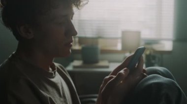 Hüsrana uğramış genç bir adamın eline telefon alıp, dizlerine sarılıp, kafasını onlara dayadığı yakın plan görüntüsü.