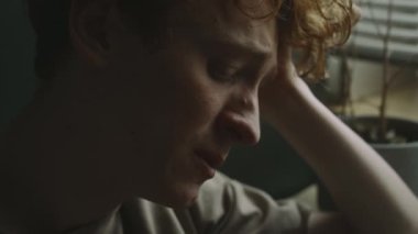 Evde ağlamak üzere olan ve sigara içen endişeli genç adamın yakın plan görüntüsü.