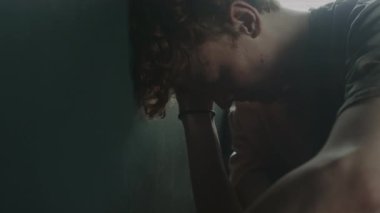 Umutsuz bir gencin kafasını koyu gri duvara vurduğunu, yumruğuyla duvarı yumrukladığını ve gözleri kapalıyken avuç içiyle ittiğini yakın plan görüntüsü.