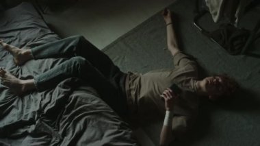 Sırtüstü uzanmış, bacakları yapılmamış yatağa fırlatılan, telefonu tutan, sonra yana dönen, bileğine sarılı beyaz bandajlı genç bir adam.