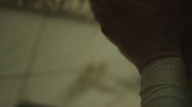 Bileğinde bandaj olan, aynanın önünde yüzünü yıkayan, burnundan aşağı süzülen genç adamın yakın görüntüsü.