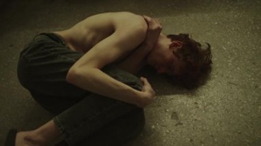 Dizleri göğsüne ve koluna kadar dizlerine kadar dizlerinin üzerine çökmüş, zihinsel olarak mücadele eden genç bir adam.