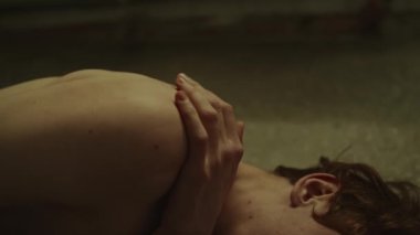 Yakından bakınca omuzlarına dokunan ve ağlayan genç bir adam cenin pozisyonunda dizleri çizilmiş bir şekilde yerde yatıyor.