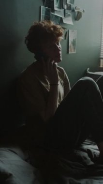 Gergin genç bir adamın telefonda duygusal konuşması, aramasının bitmesi ve evde ağlamasının dikey görüntüsü.