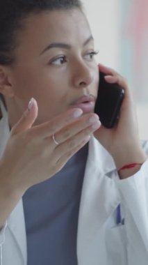 Tıp kürklü genç bir kadın doktorun klinikteki iş yerinde cep telefonuyla sohbet ederken dikey pozu.