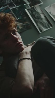 Hüsrana uğramış genç bir adamın dikey bakış açısı yastığa sarılıp çenesini kapatması, sonra da kafasını yatak odasındaki duvara doğru çekmesi.