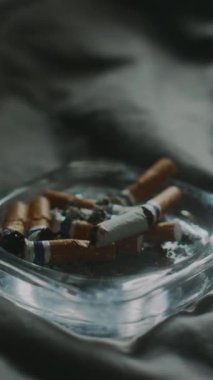 Yatak odasında sigara içtikten sonra camdan kül tablasına sigara koyan tanımadığım bir adamın dikey yakın çekimi.