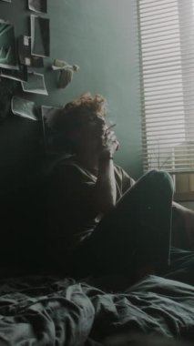 Yatağında dağınık bir şekilde sigara içen stresli bir gencin dikey görüntüsü.