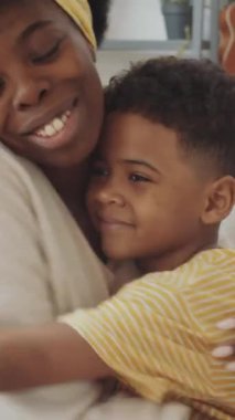 Afro-amerikan genç annesini sevmenin dikey yakın çekimi. Küçük oğluna şefkatle sarılıyor ve kameraya bakıyor.