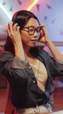 Genç Asyalı bir kadının mikrofona kulaklık takıp konuştuğu dikey bir görüntü.