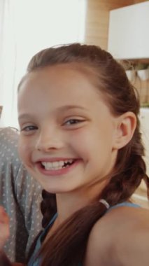 Bir yandan gülümseyen kızın kameraya el sallarken diğer yandan ablasıyla birlikte tatilde ailesiyle birlikte otururken çekilmiş dikey yakın çekim görüntüleri.