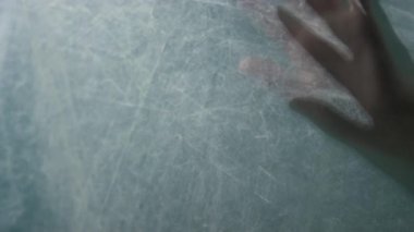 Kırışık polietilen film ve birbirine geçmiş parmaklar üzerinde hareket eden bulanık ellerin yakın plan çekimi.